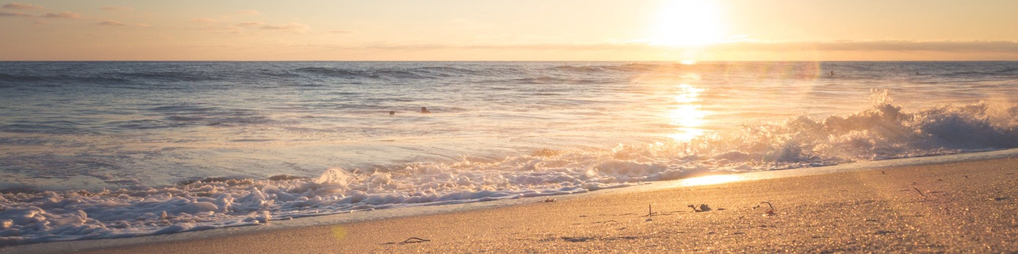 A tranquil beach scene at sunset, with gentle waves lapping onto the sandy shore and the sun casting a warm, golden glow over the horizon.