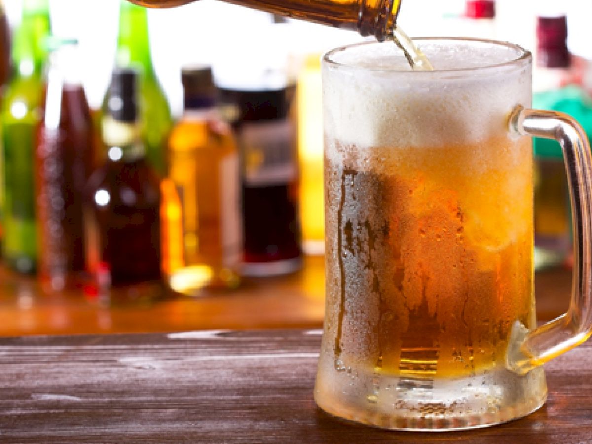 A beer is being poured into a chilled mug with a foamy head, surrounded by various bottles in the background.