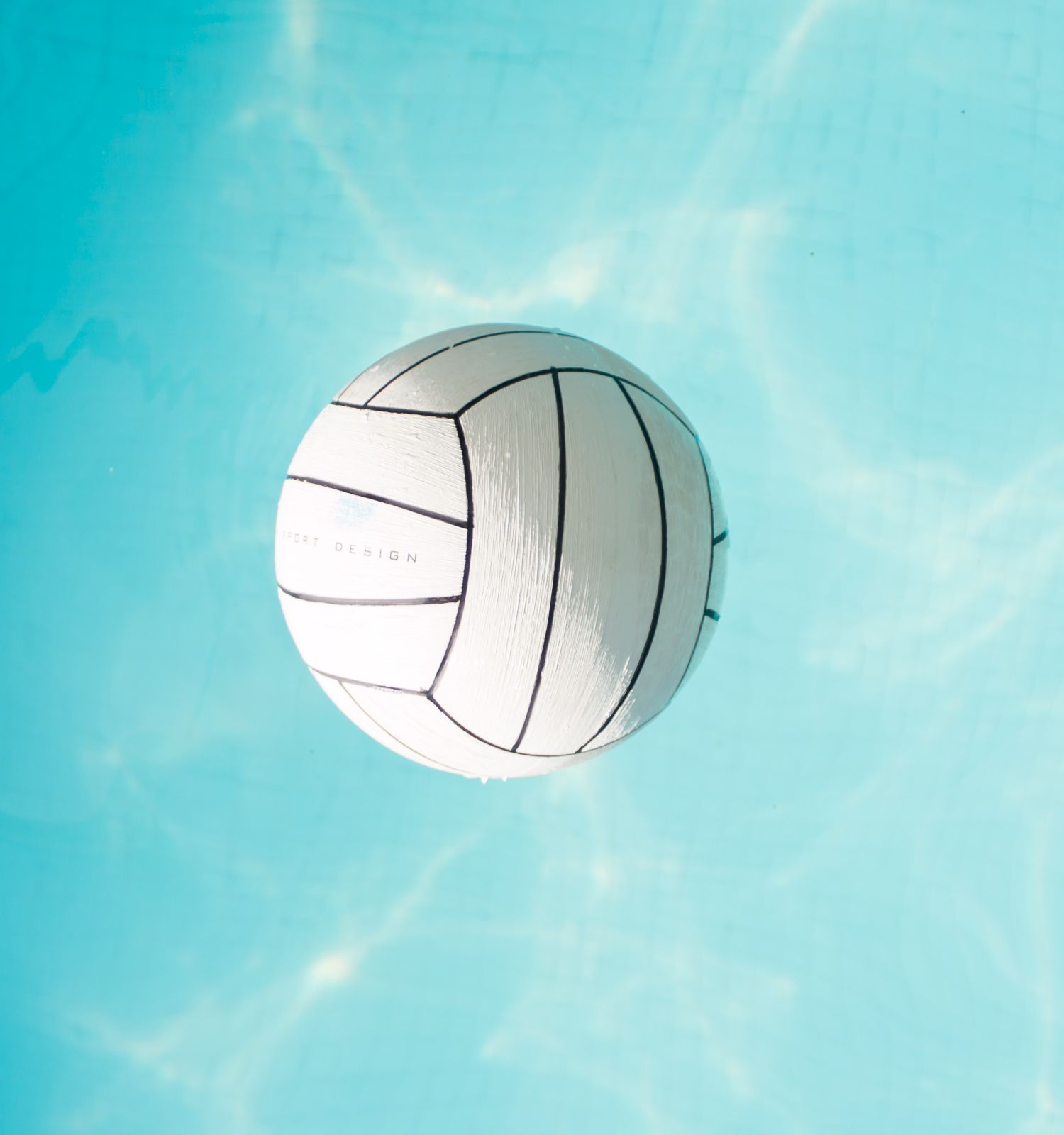 A white volleyball floating on clear, blue water with sunlight reflecting on the surface, creating a serene and bright scene.