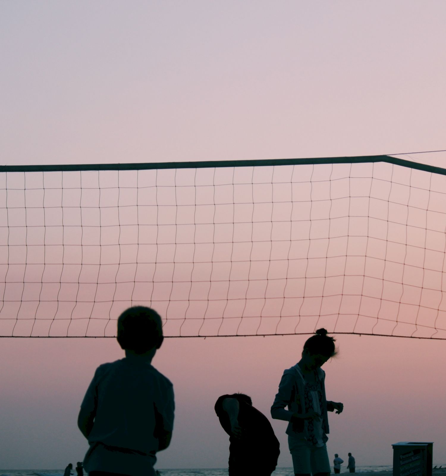 Silhouettes of people near a volleyball net at sunset on a beach.