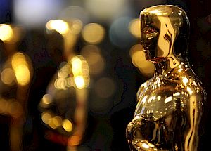 The image shows several golden Oscar statuettes standing in focus against a blurred background.