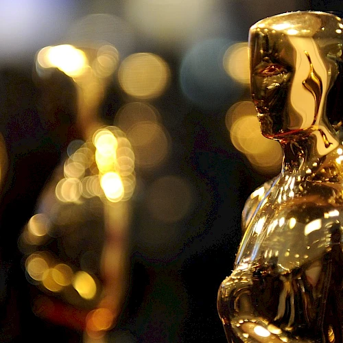 The image shows several golden Oscar statuettes standing in focus against a blurred background.