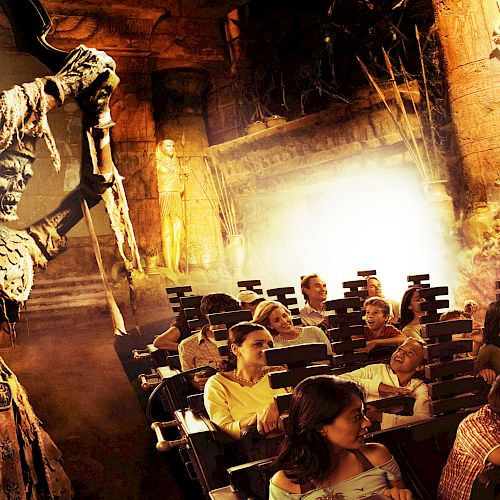 A group of people on an amusement park ride themed around a skeleton warrior wielding a weapon in a fiery, ancient temple setting.