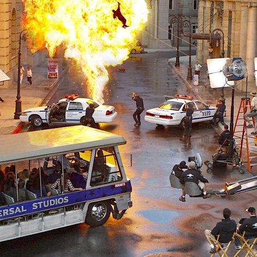 Movie set scene with explosion, cop cars, crew operating cameras, and onlookers on a Universal Studios tour tram.