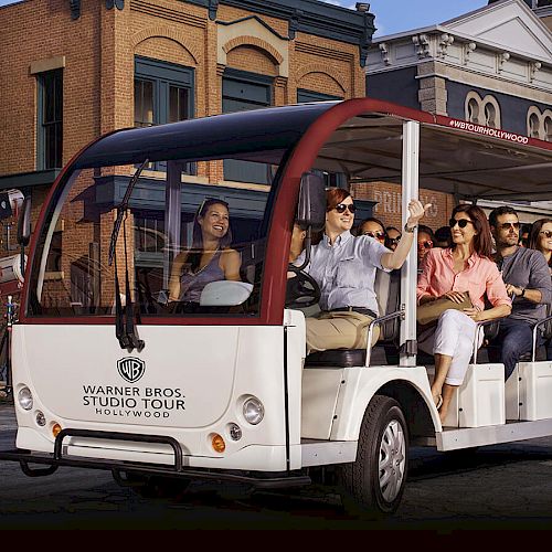 A group of people in a tour tram at Warner Bros. Studio Tour Hollywood, enjoying the ride through a set resembling an old town area.
