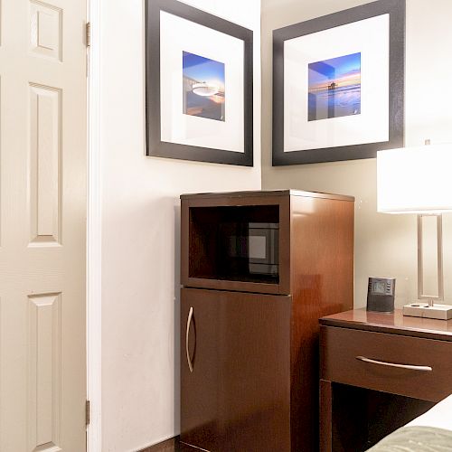 A cozy corner of a room with a microwave on a cabinet, a lamp on a nightstand, and two framed pictures on the wall above it, ending the sentence.