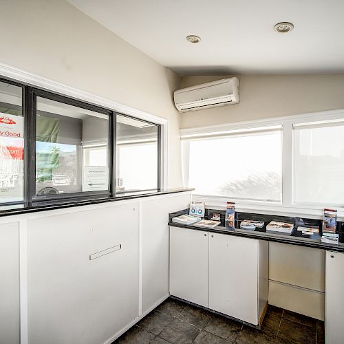 An office reception area with a counter, brochures, windows, and an air conditioning unit on the wall.