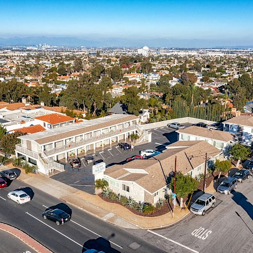 An aerial view of a suburban neighborhood with multiple buildings, vehicles on the street, and a wide cityscape in the background ending the sentence.