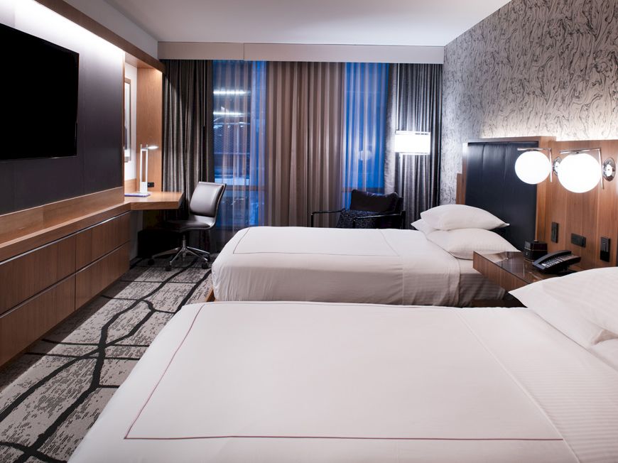 This image shows a modern hotel room with two neatly made beds, a desk with a chair, a flat-screen TV, and contemporary decor ending the sentence.