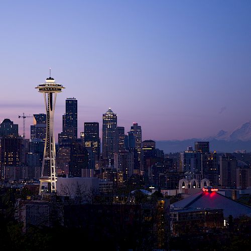 The image shows a scenic view of Seattle's skyline at twilight, featuring the Space Needle prominently with Mount Rainier in the background.