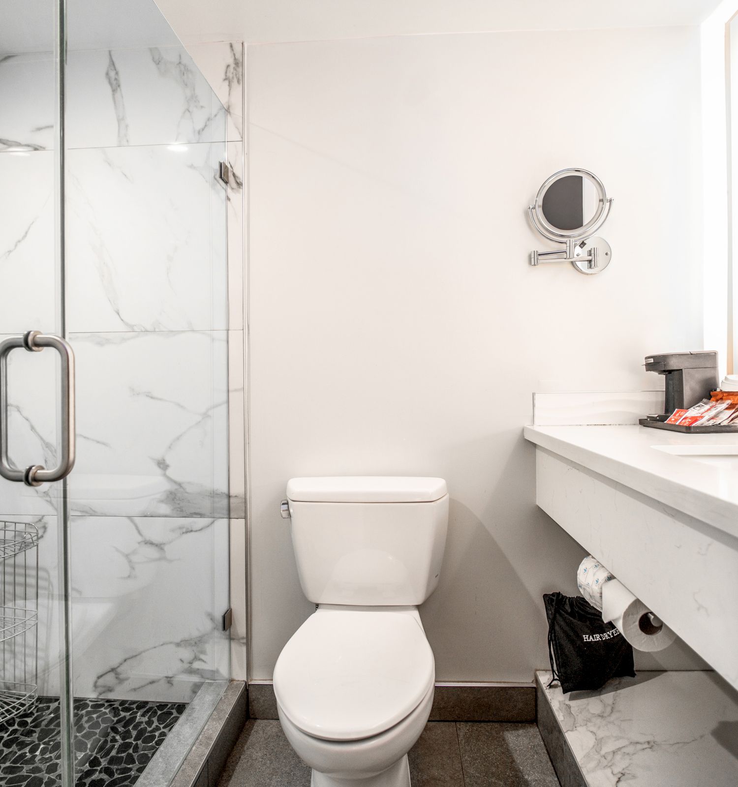 A modern bathroom features a glass shower, a toilet, a white marble countertop with a sink, and a mounted mirror.