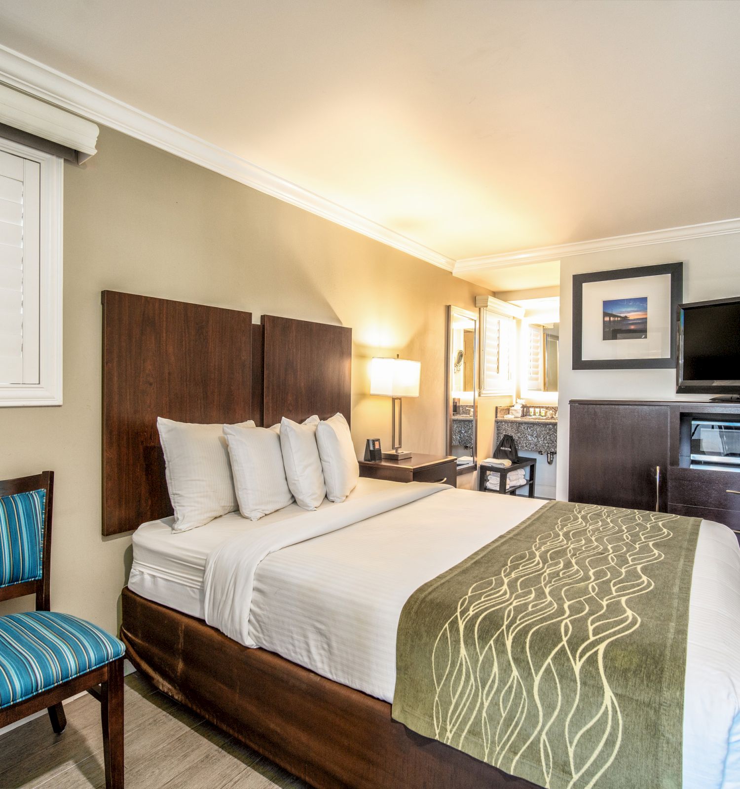 A cozy, modern hotel room featuring a bed, a chair, a television, a microwave, and wall art, with a bright, inviting ambiance.